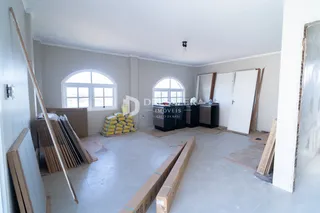 Interior de uma sala em construção com paredes brancas e janelas arqueadas.