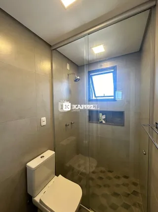 Foto interna de um banheiro com box de vidro e vaso sanitário.