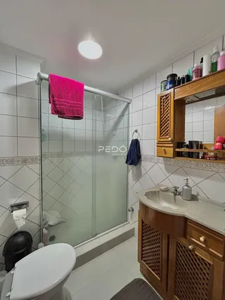 Foto interna de um banheiro com box de vidro e revestimento cerâmico.