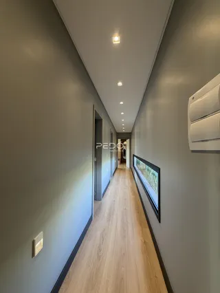 Corredor interno de uma residência com piso de madeira clara e paredes cinzas.