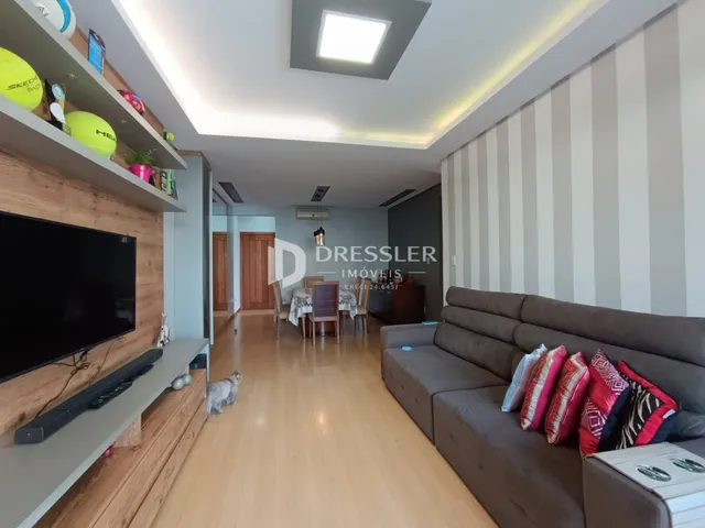 Vista interna de uma sala de estar com piso de madeira clara e móveis modernos.