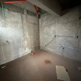 Foto de um ambiente interno com paredes de concreto aparente e piso cru.