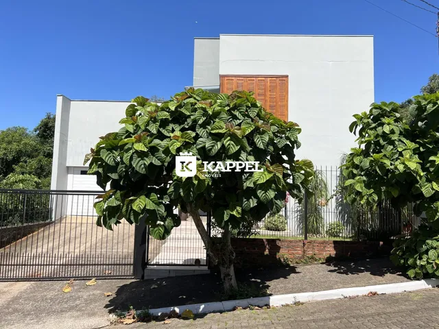 Fachada de uma residência moderna em Lajeado, Brasil, com vegetação exuberante no primeiro plano.