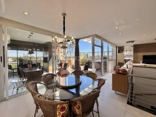 Sala de jantar com mesa de vidro e cadeiras de vime em um apartamento.