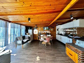 Sala de estar com pé direito alto e cozinha integrada em ambiente com piso de madeira.