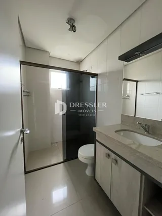Interior de um banheiro com piso claro e divisória de vidro.