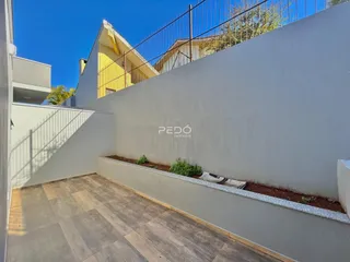 Área externa com piso de cerâmica e muro branco.