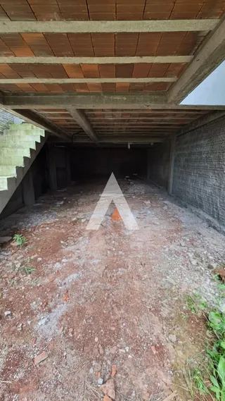 Foto de um espaço interno com piso de terra e teto de concreto.