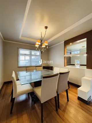 A sala de jantar apresenta uma mesa de vidro com cadeiras brancas e piso de madeira.