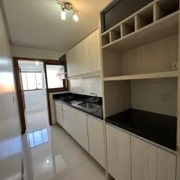 Uma cozinha com armários brancos e bancada escura é visível na foto.