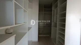 Vista interna de um corredor com estantes brancas e paredes claras.