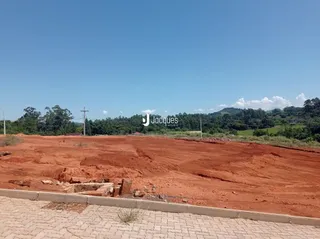 Vista do terreno com solo avermelhado sob céu azul.