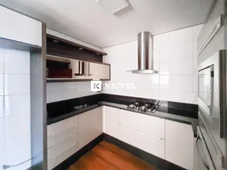 Cozinha com armários brancos, bancadas escuras e exaustor de aço inoxidável.