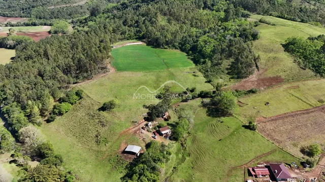 Vista aérea de uma propriedade rural com campos verdes e vegetação densa.