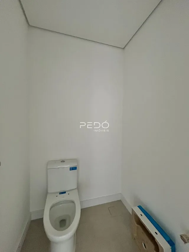 Vista de um corredor interno com um vaso sanitário branco e paredes brancas.