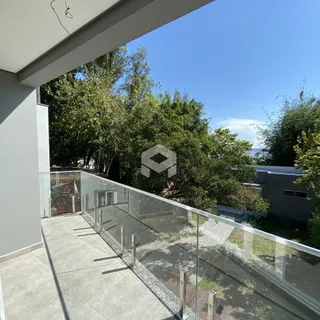 Vista de uma varanda com grade de vidro e vegetação ao fundo.