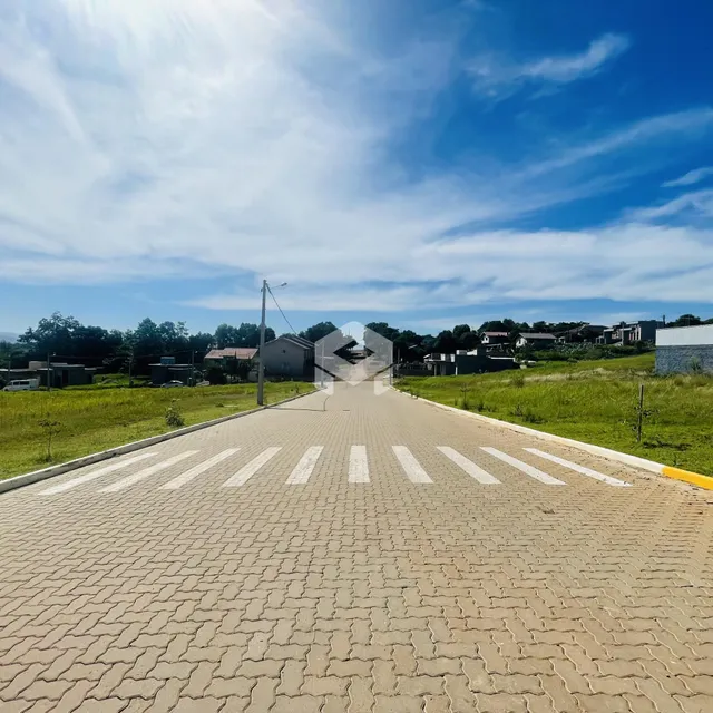 Uma estrada pavimentada com faixas de pedestres se estende por uma área gramada com casas ao fundo.