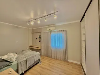 Quarto com cama e janela coberta por cortinas claras.