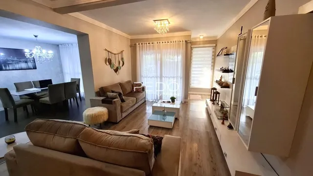 Sala de estar com piso de madeira e sofá de cor bege.