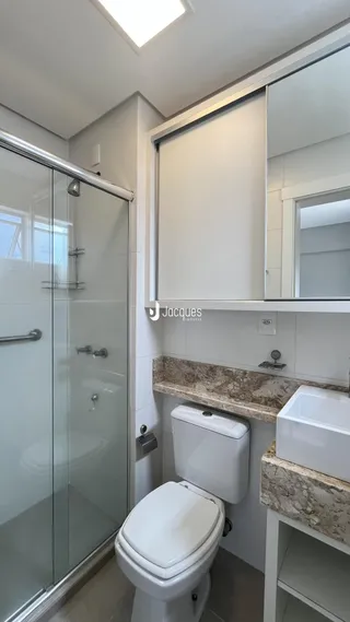 Foto interna de um banheiro com box de vidro e louças brancas.