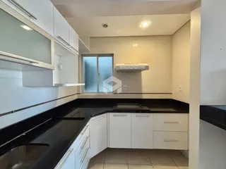 Interior de uma cozinha com armários brancos e bancadas pretas.