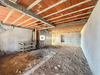 Interior de um espaço em construção com estrutura de madeira exposta e piso de terra.