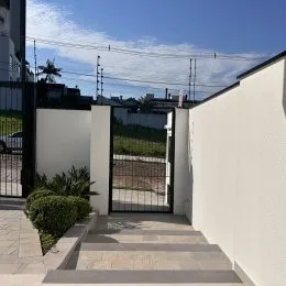 Foto da fachada de uma residência com muro branco e portão de metal.