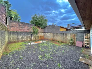 Vista externa de um quintal com muro de tijolos e vegetação.