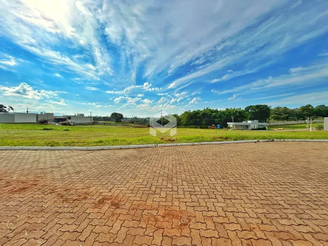 Vista externa de um terreno com gramado e área pavimentada sob um céu azul e nublado.