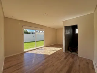Uma sala ampla com piso de madeira e porta de vidro que dá acesso a um gramado.