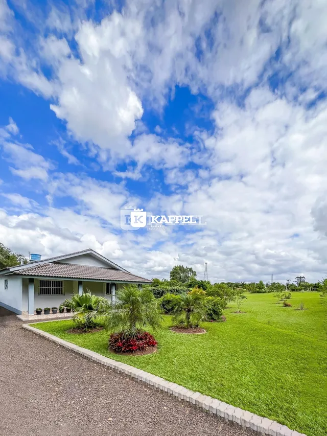 Foto da fachada de uma casa com jardim verde e campo aberto ao fundo.