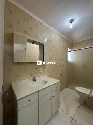 Banheiro com bancada branca e revestimento de azulejos claros.