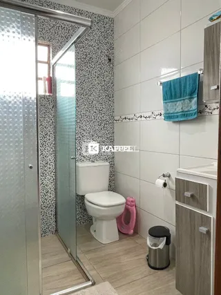 Banheiro com revestimento de azulejos e box de vidro transparente.