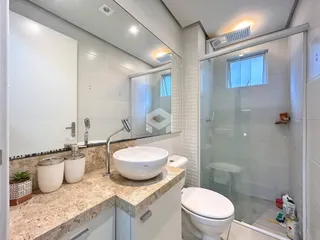 Banheiro com bancada de granito e box de vidro transparente.