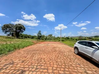 A foto mostra uma área externa pavimentada com tijolos vermelhos e um campo verde ao fundo.