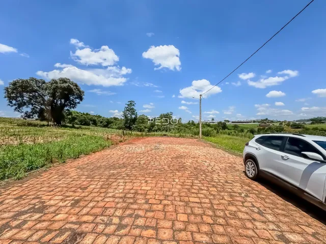 A foto mostra uma área externa pavimentada com tijolos vermelhos e um campo verde ao fundo.