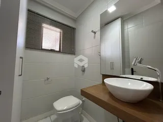 Banheiro com revestimento cerâmico branco e bancada de madeira.