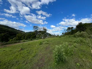 Paisagem de campo com colinas verdes sob um céu azul e nuvens.