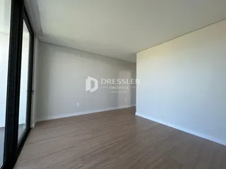 Vista interna de um ambiente com paredes brancas e piso de madeira clara.