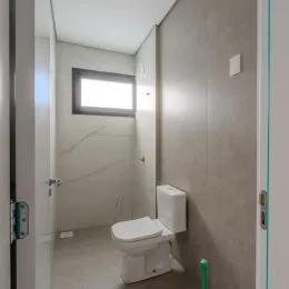 Foto interna de um banheiro com revestimento de azulejos brancos e vaso sanitário.