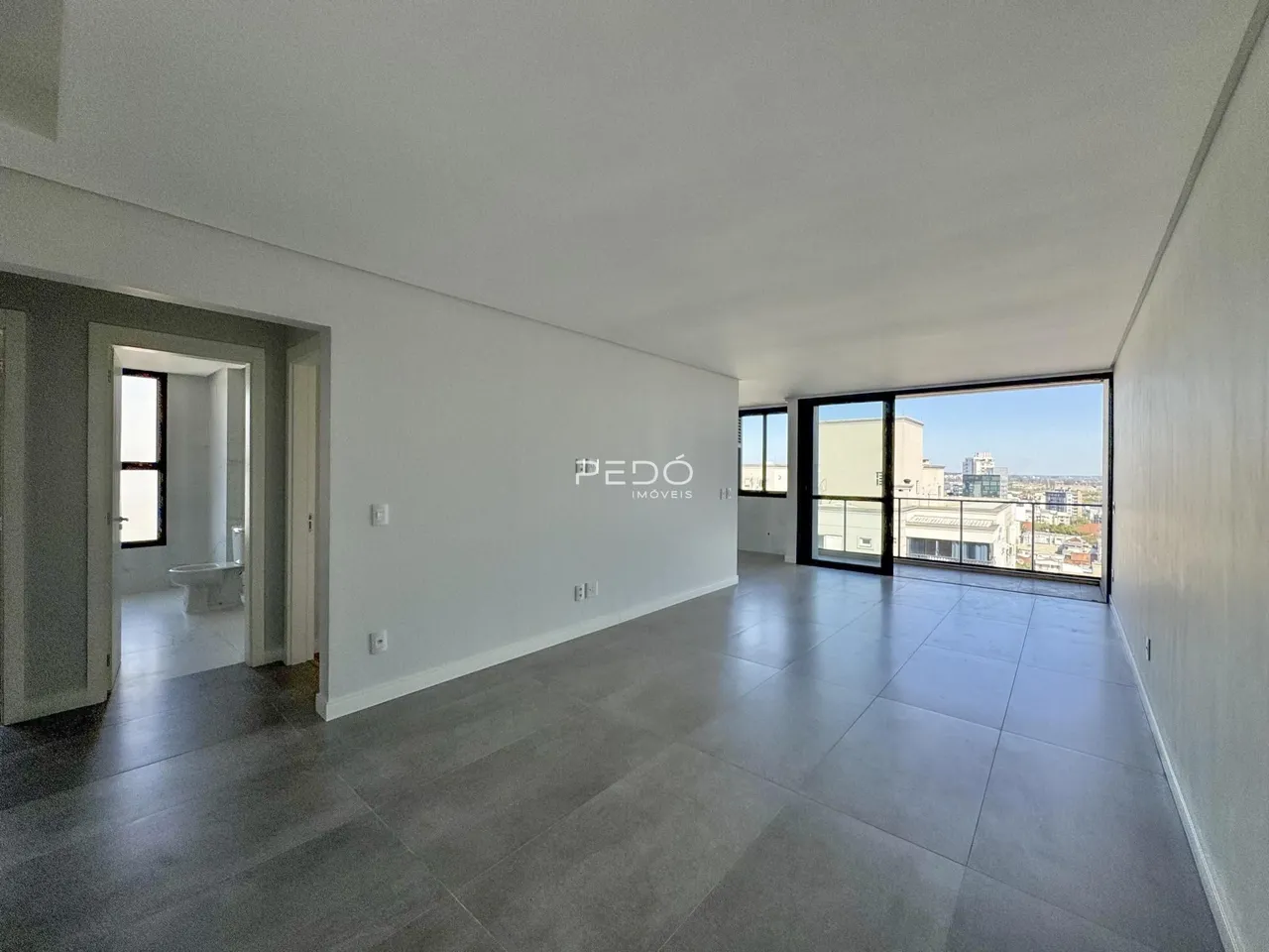 Ambiente interno de uma sala ampla com piso de cerâmica e vista para a cidade.