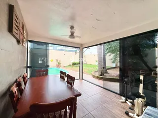 Vista de uma sala de jantar com mesa de madeira e portas de vidro que dão acesso a um pátio com piscina.