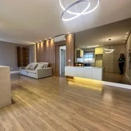 Sala de estar com piso de madeira clara e teto liso.