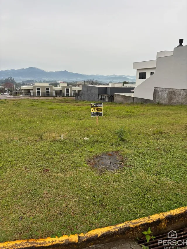 Vista externa de um terreno com grama verde e um edifício branco ao fundo.