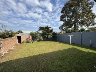 Vista de um quintal gramado com muro de tijolos e cerca.