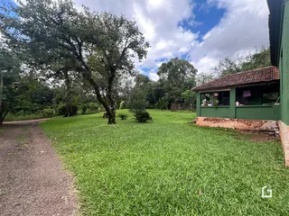 Vista externa de um terreno gramado com uma estrada de terra e uma casa ao fundo.
