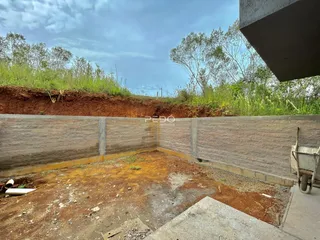 Parede de contenção de terra com vegetação ao fundo.