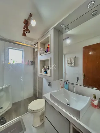 Interior de um banheiro moderno com box de vidro e bancada branca.