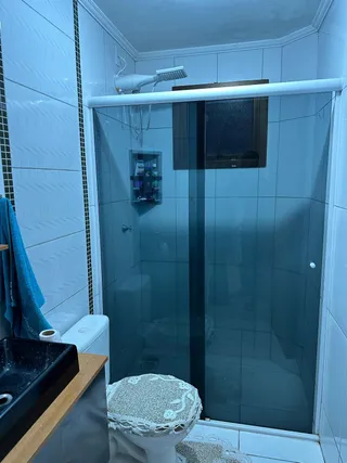 Foto interna de um banheiro com box de vidro e revestimento de azulejos brancos.
