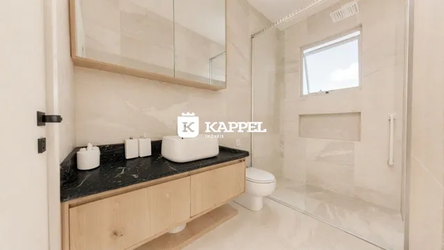 Foto de um banheiro com bancada de mármore e box de vidro transparente.